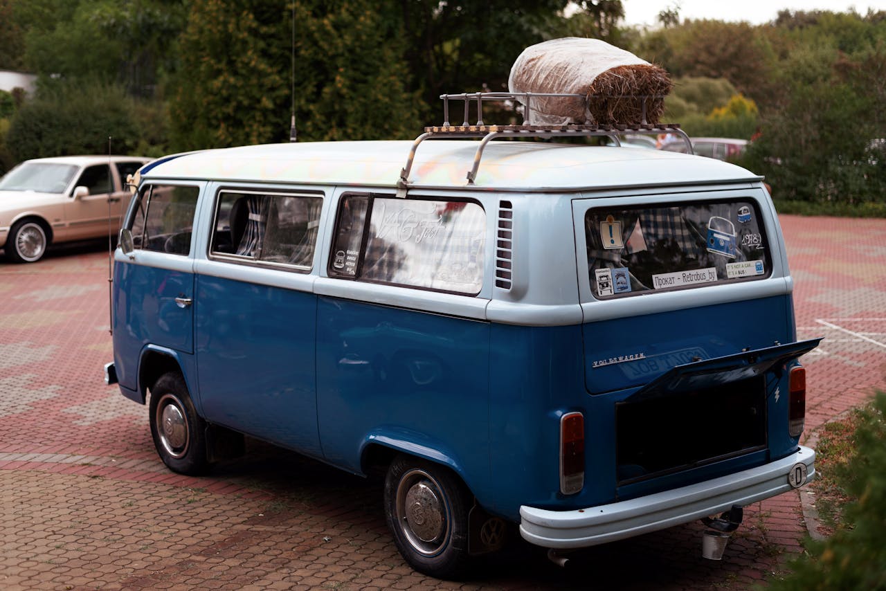 A vintage blue Volkswagen camper van parked in an outdoor setting with luggage on the roof rack.