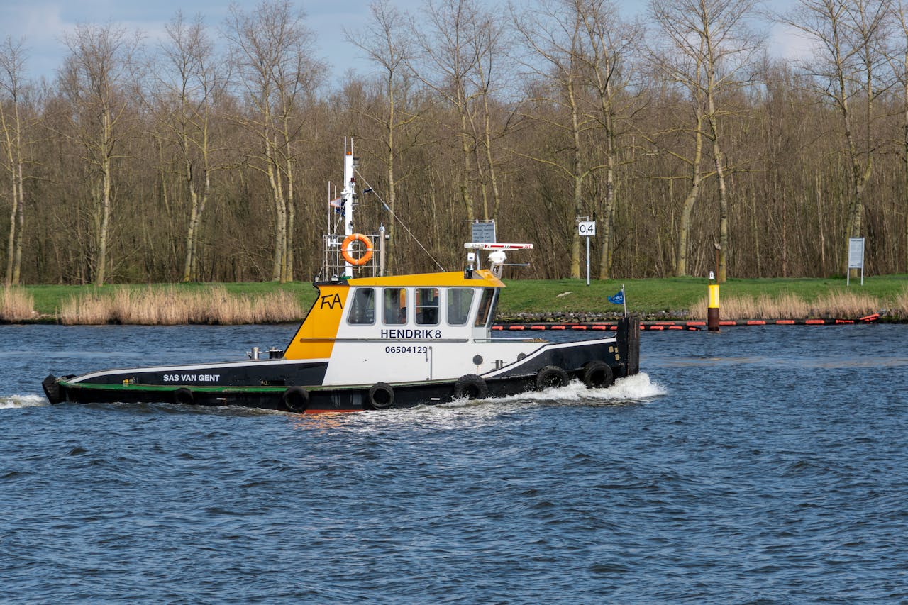 A tugboat named Hendrik 8 sails on a calm river surrounded by a forested landscape.