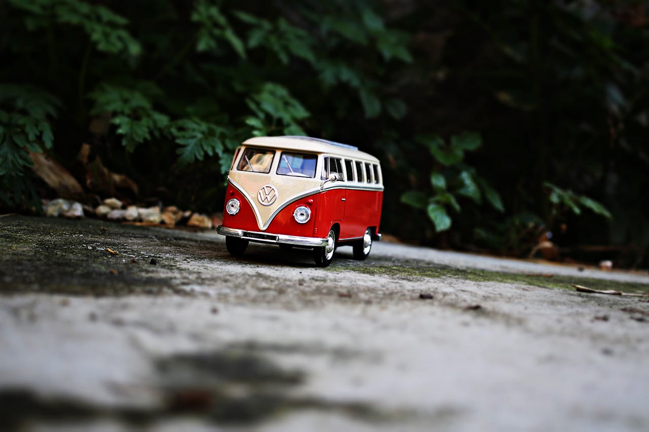Charming classic red toy van on paved ground, amidst outdoor greenery.