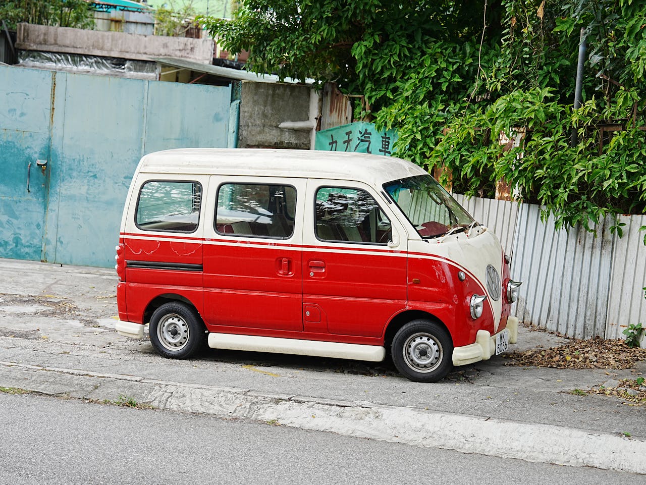 Classic red and white van parked on a street with greenery in the background.